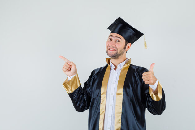 成功年轻人竖起大拇指 穿着毕业制服 脸上露出高兴的神情 正对着前方聪明衬衫指点