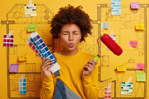 年轻人家庭主妇嘴唇圆润 忙着装修房子 拿着画笔和调色板 根据设计方案在公寓里修缮油漆工在黄色墙上的素描上摆姿势房子选择美式