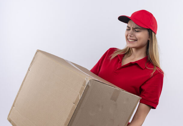 手势紧张的年轻送货女孩穿着红色制服 戴着帽子 手里拿着沉重的箱子 孤零零地站在白色的地板上帽子女人制服