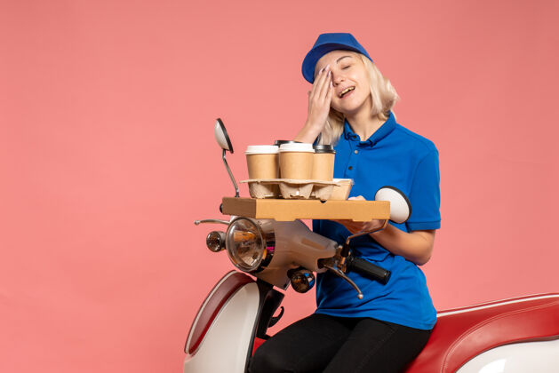 漂亮正面图骑自行车的女快递员 咖啡杯放在粉红色的椅子上工人制服杯子