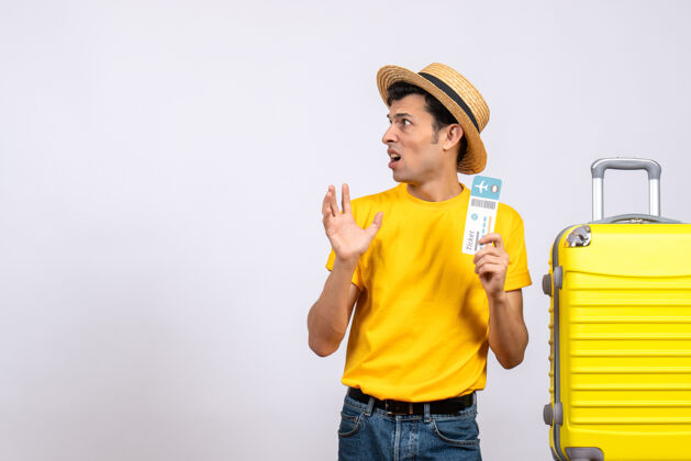成人前视图困惑的年轻人穿着黄色t恤站在黄色手提箱旁边拿着票抱着可爱微笑