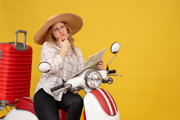 车辆俯视图是一个戴着帽子 坐在摩托车上 拿着地图的年轻女子 集中在黄色的东西上摩托车集中举行
