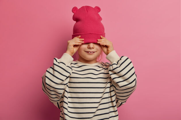 小《快乐女婴》的独立镜头露出两颗牙齿 戴着时髦的帽子遮住眼睛 穿着休闲的条纹套头衫 到处游荡 只是快乐 隔离在粉色的墙上孩子的时尚理念高兴幼儿园脸