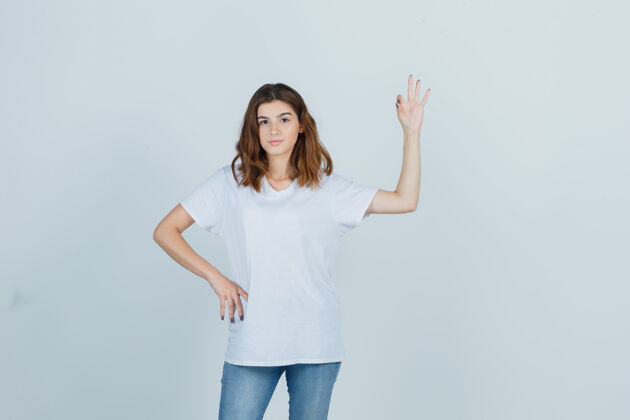 成人在白色t恤 牛仔裤和看起来自信的前视图显示ok手势的年轻女孩的肖像自信女士女孩