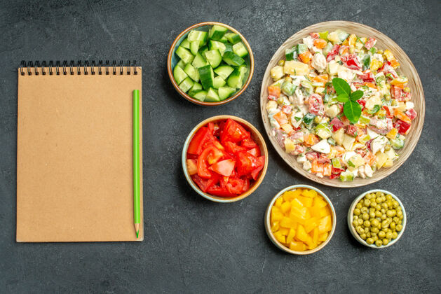 料理一碗蔬菜沙拉的俯视图 在深绿色背景上 有一碗蔬菜和一个侧边有笔的记事本深色午餐美味