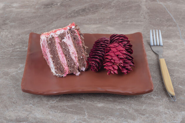 美味一块蛋糕和红松球果放在一个盘子里 旁边是一个大理石叉子烘焙口感蛋糕