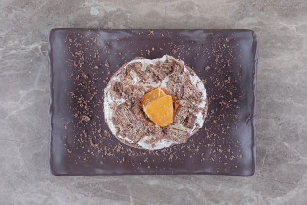 甜点在大理石上的盘子上放一个小蛋糕 上面有切碎的橘子馅糖蛋糕奶油