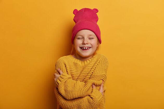 童年快乐小女孩儿的横拍拥抱自己 感觉温馨 戴着粉色帽子和针织毛衣 精神高昂 隔着黄色的墙壁孩子们 自尊年轻我自己女孩