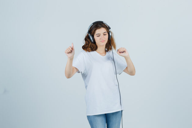头发穿着白色t恤 牛仔裤 戴着耳机欣赏音乐的年轻女性的肖像 看上去很快乐卷发牛仔裤微笑