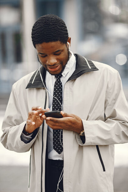 公司优雅的非裔美国人站在街上用带耳机的手机企业家领带城镇