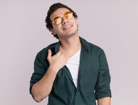 站立身穿绿衬衫 戴着眼镜的年轻人站在白墙上 脸上带着自信的表情 抚摸着自己的脖子自信眼镜衬衫