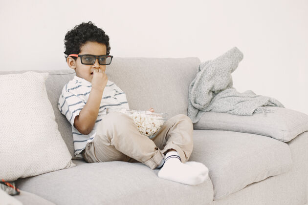 天吃爆米花的男孩在玻璃里的非洲男孩看儿童电影沙发房子微笑