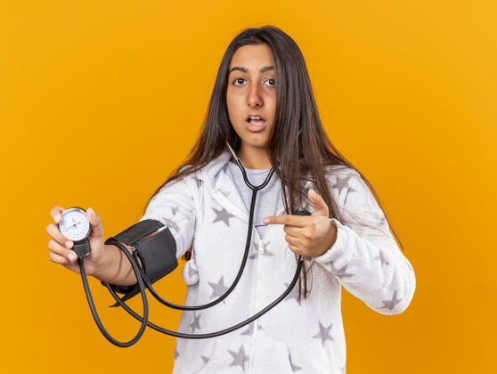 自己被吓坏了的年轻病女孩用隔离在黄色背景上的血压计测量自己的血压衡量疾病女孩