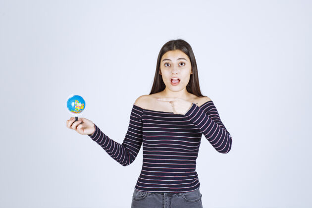 地图穿着条纹衬衫的女孩拿着一个迷你地球仪指着它学习工人成人