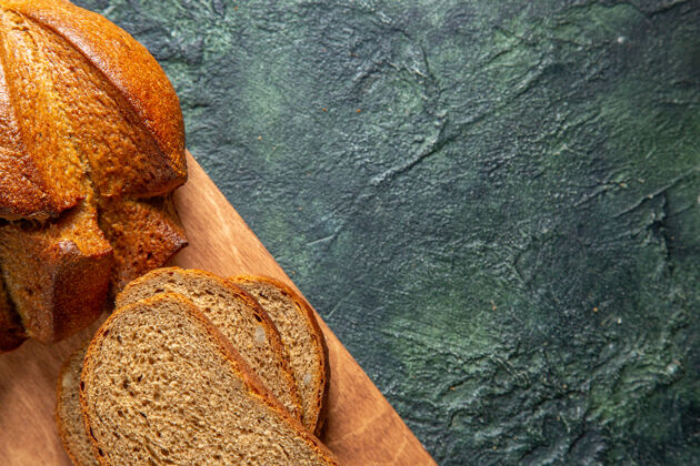早餐在深色背景的棕色木砧板上拍摄半张完整的黑面包新鲜木板一半