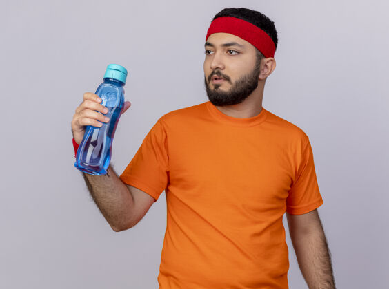 运动思考年轻的运动型男子一边看着戴着头带和手环拿着水瓶隔离在白色背景上持有瓶子壁板