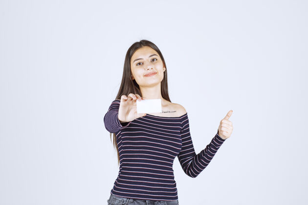 员工穿条纹衬衫的女孩拿着名片 举着拇指朝上的牌子成功年轻雇员