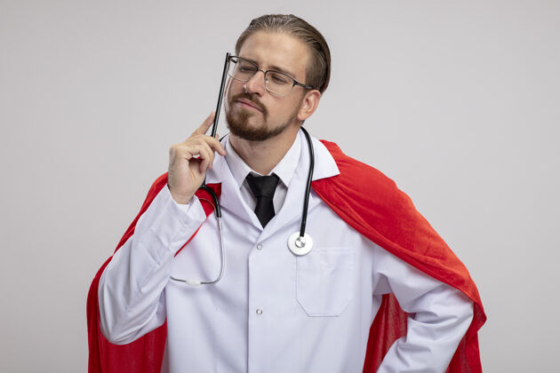 超级英雄年轻的超级英雄穿着医用长袍 戴着听诊器和眼镜 把铅笔贴在脸颊上 隔离在白色背景上长袍铅笔眼镜