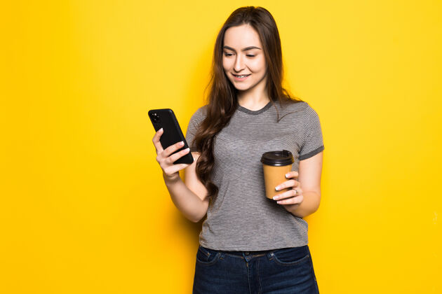 女孩年轻女子用电话把咖啡杯隔在黄色的墙上钱包手机电话
