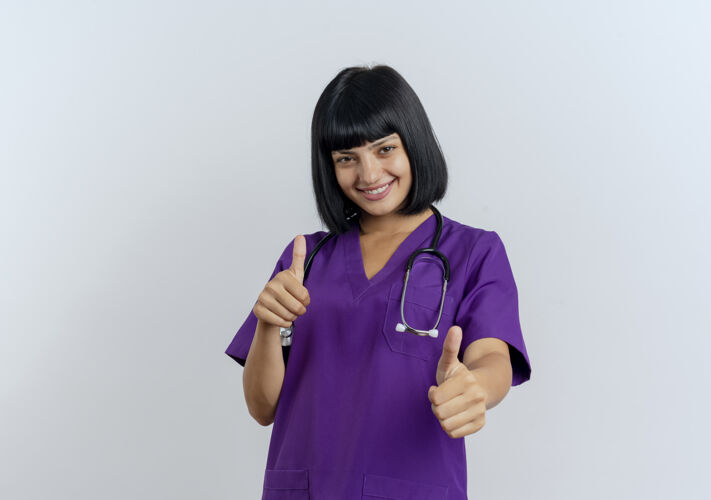 制服微笑的年轻黑发女医生穿着制服 双手竖起听诊器大拇指手女拇指