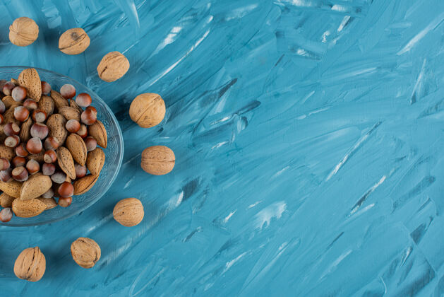 坚果在蓝色背景上放满各种健康新鲜坚果的玻璃盘子可口核桃碗