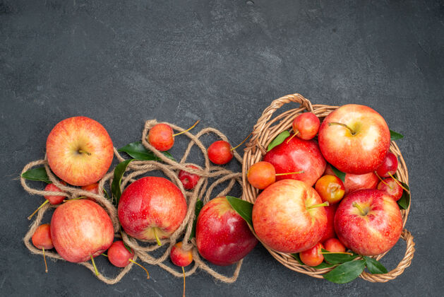 樱桃从远处俯瞰苹果开胃的苹果樱桃在篮子绳子上放在黑暗的桌子上可食用水果多汁水果