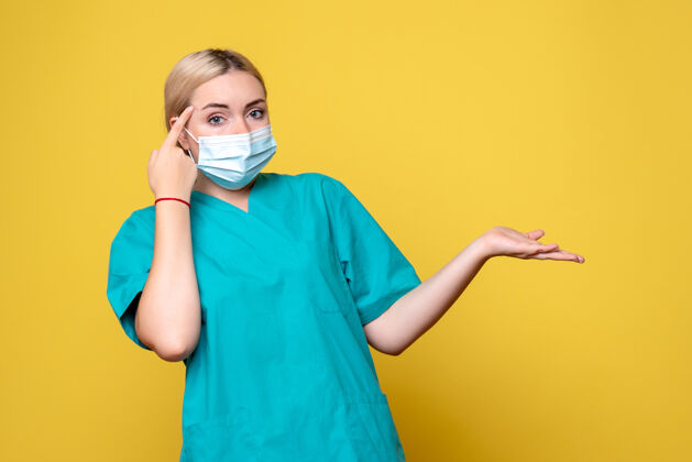正面黄色墙壁上穿着医用衬衫和无菌口罩的年轻女医生的正面图大流行医疗护士