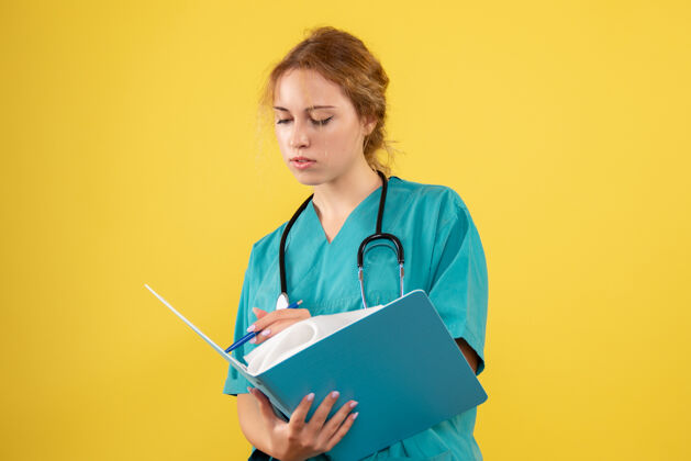 纸张黄色墙壁上穿着医疗服的女医生带着论文和分析的正视图人女医生正面