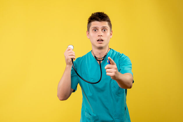人黄色墙壁上穿着带听诊器的医疗服的男医生的正视图前面病毒听诊器