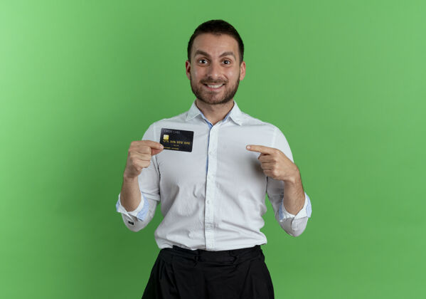 点笑容可掬的帅哥拿着信用卡指着隔离在绿色墙上的墙人绿色成人