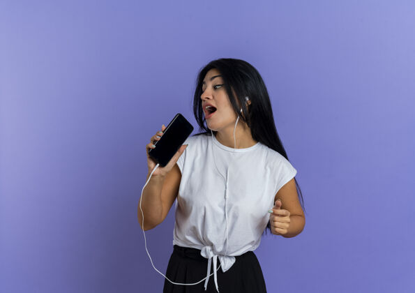 壁板快乐的年轻白人女孩戴着耳机拿着电话假装在一旁唱歌假装紫色年轻