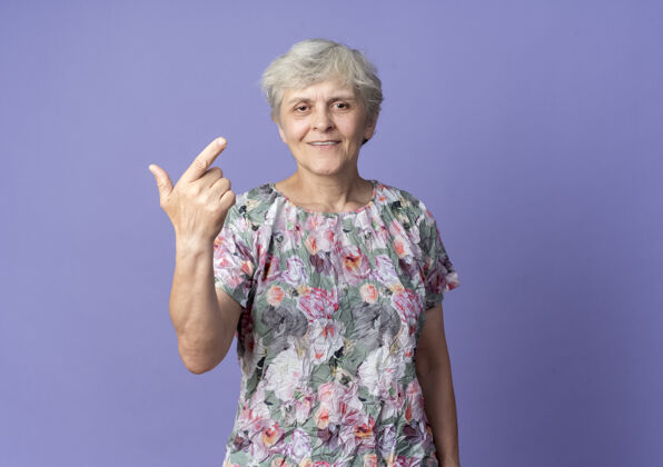 枪微笑的老妇人手势标志孤立在紫色的墙上微笑女人手势