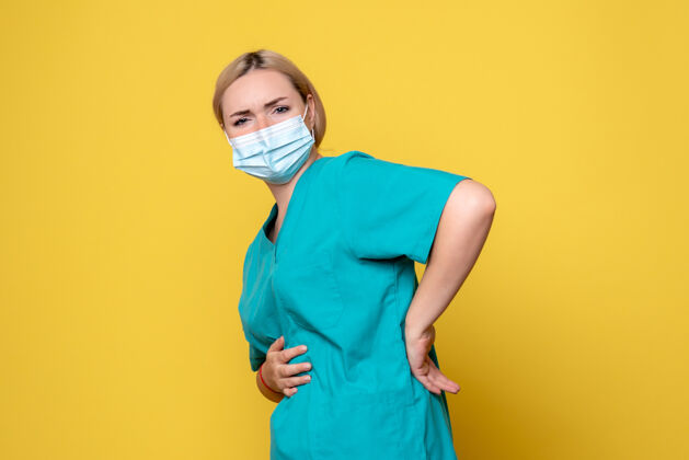 年轻女医生黄色墙壁上穿着医用衬衫和无菌口罩的年轻女医生的正面图西装面具成人