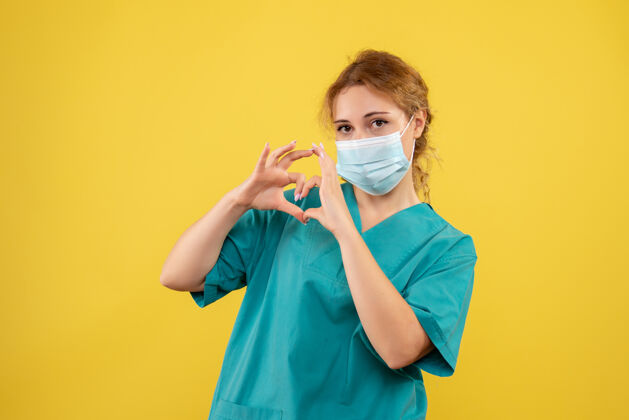 成人身着医疗服 戴着无菌口罩的年轻女医生的正面图 黄色墙上显示着爱的标志医疗护士绝育