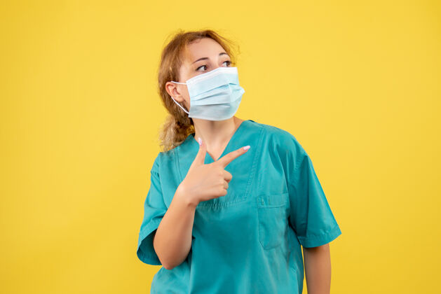 面具黄墙上穿着医疗服 戴着无菌口罩的女医生的正面图健康大流行人