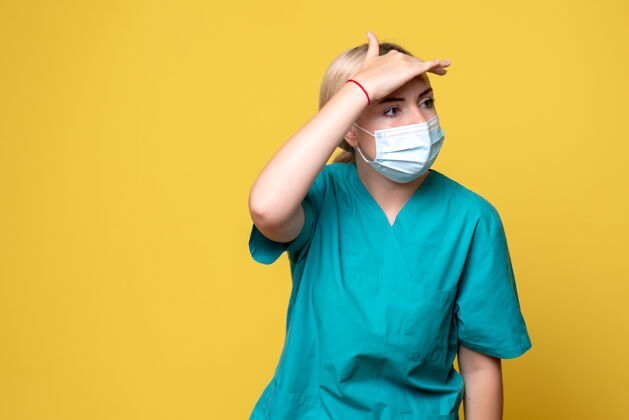 医院黄色墙壁上穿着医用衬衫和无菌口罩的年轻女医生的正面图人年轻女医生医疗