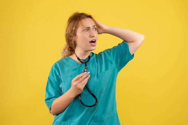 医疗黄色墙壁上穿着带听诊器的医疗服的女医生的正视图人仪器病毒