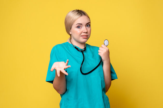 医院黄色墙壁上穿着带听诊器的医用衬衫的女医生的正视图器械护士健康