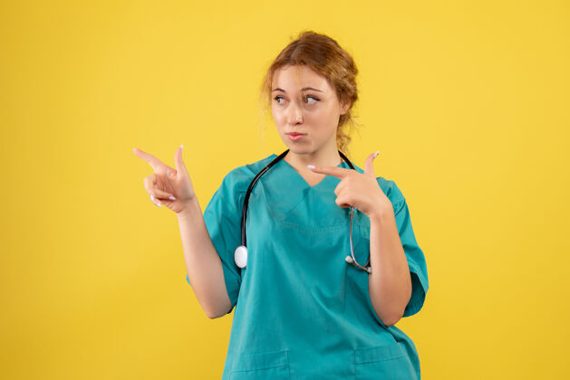 人黄色墙壁上穿着带听诊器的医疗服的女医生的正视图成人人前面