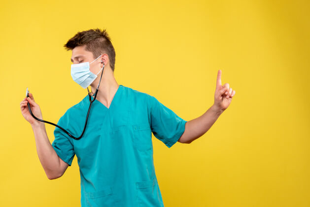 男性黄色墙壁上穿着医疗服 戴着听诊器面罩的男医生的正视图人肖像成人