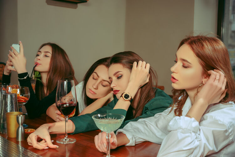 网络在酒吧喝饮料的女性朋友 她们坐在一张摆着鸡尾酒的木桌旁 穿着休闲服酒吧悲伤人