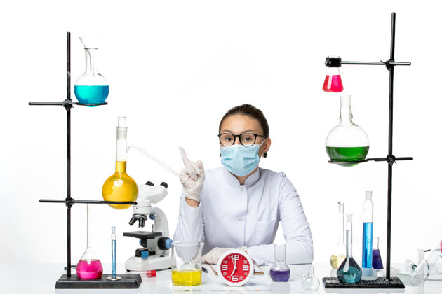 医学前视图穿着白色医疗服的女化学家 戴着面具坐在白色背景上化学家病毒冠状病毒-飞溅实验室坐着面具套装