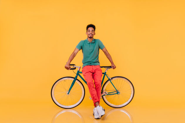 非洲自信的非洲男子站在自行车前的全长肖像一个情绪化的黑人穿着鲜艳的衣服和自行车合影情绪自行车快乐