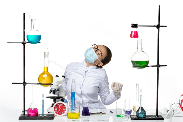 容器前视图穿着医疗服的女化学家戴着面具痛苦地躺在白色背景上病毒化学实验室的covid飞溅物上设备疼痛瓶子