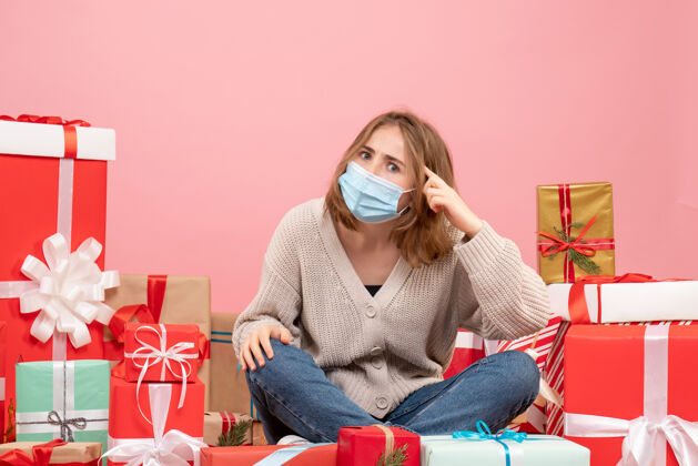 年份正面图：坐在圣诞节周围的年轻女性戴着无菌面具出现礼物房子消毒