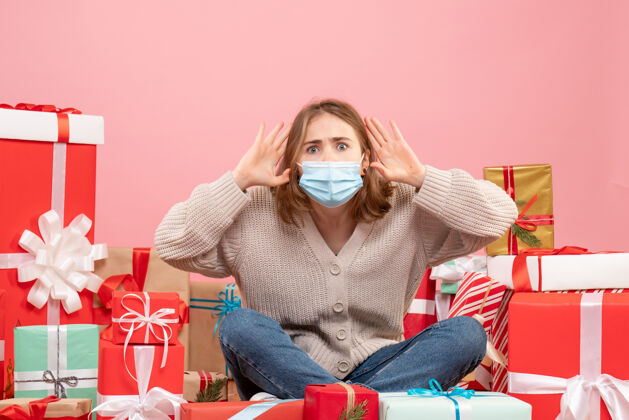 病毒正面图：坐在圣诞节周围的年轻女性戴着无菌面具出现绝育成人圣诞节