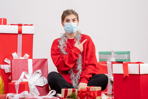 微笑正面图：年轻女性戴着无菌面具坐着 手里拿着圣诞礼物绝育坐着礼物