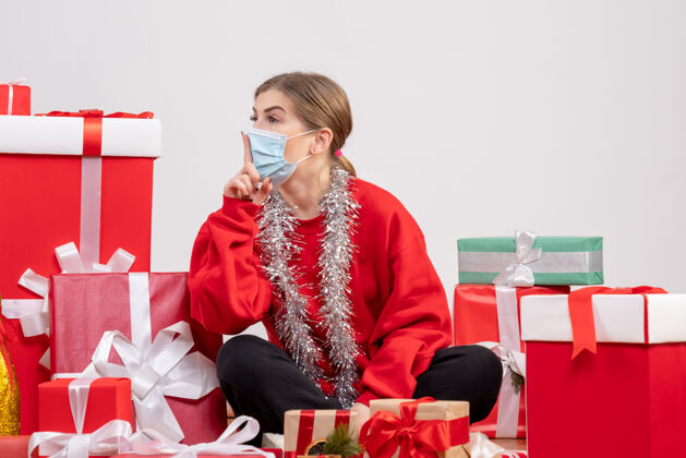 健康正面图：年轻女性戴着无菌面具坐着 手里拿着圣诞礼物生活坐着消毒