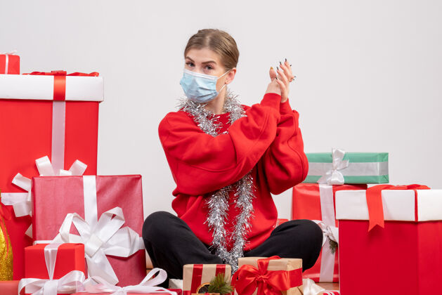 健康正面图：年轻女性戴着无菌面具坐着 手里拿着圣诞礼物病毒快乐坐着