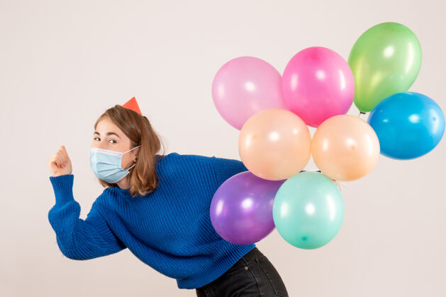 生日正面图：戴着消毒面具的年轻女性手持五颜六色的气球举行圣诞节乐趣